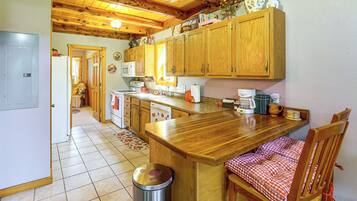 A kitchen with wooden cabinets, a stainless steel trash bin, a checkered chair, and a tiled floor.