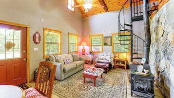 A cozy living room with a fireplace, a wooden ceiling, and a stone wall.