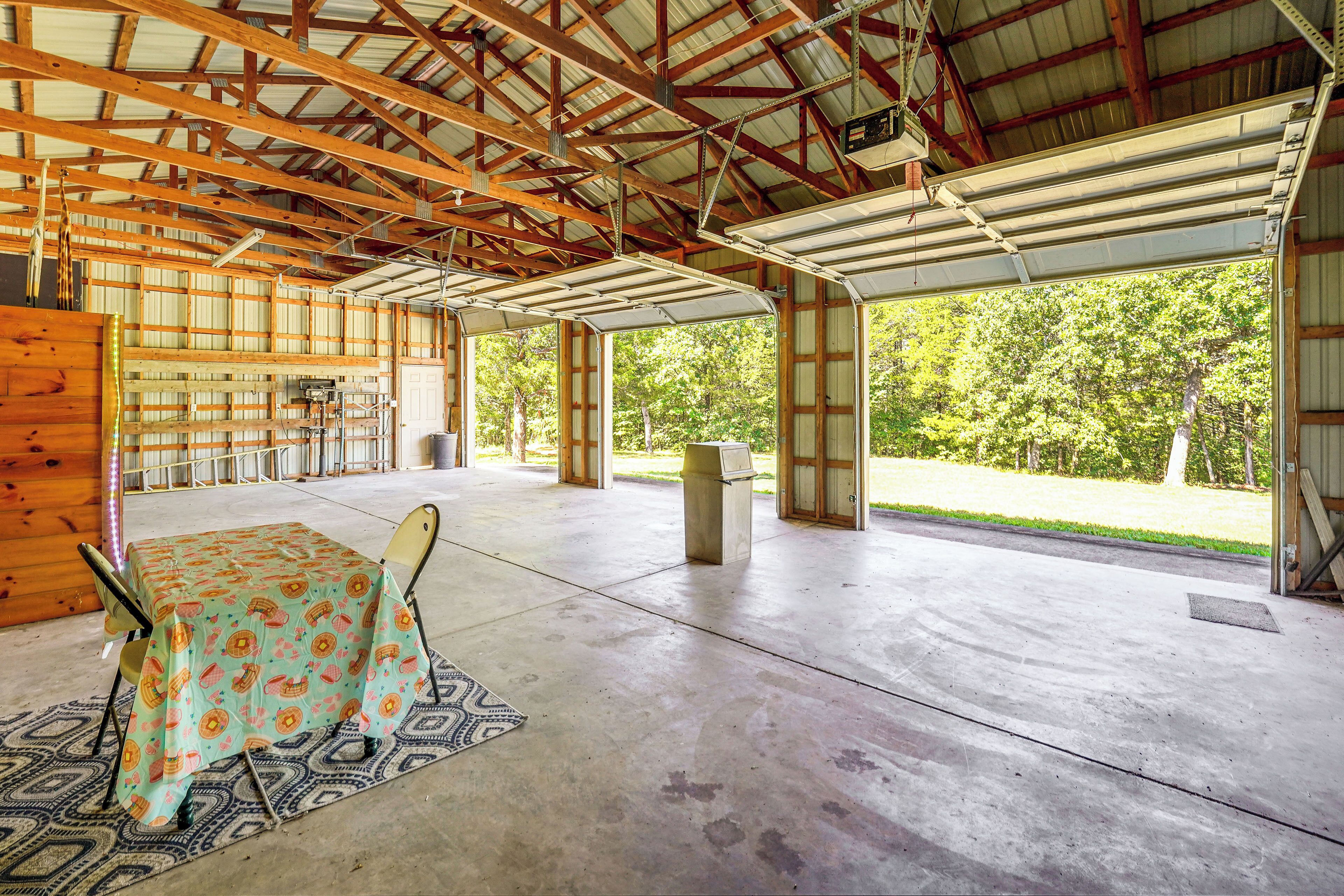An open-plan structure with a concrete floor, wooden beams, and a covered area with a table and chairs.