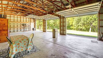 An open-plan structure with a concrete floor, wooden beams, and a covered area with a table and chairs.