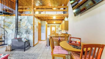 Un interior rústico con pared de piedra, vigas de madera en el techo, un comedor con mesa y sillas, y una cocina al fondo.