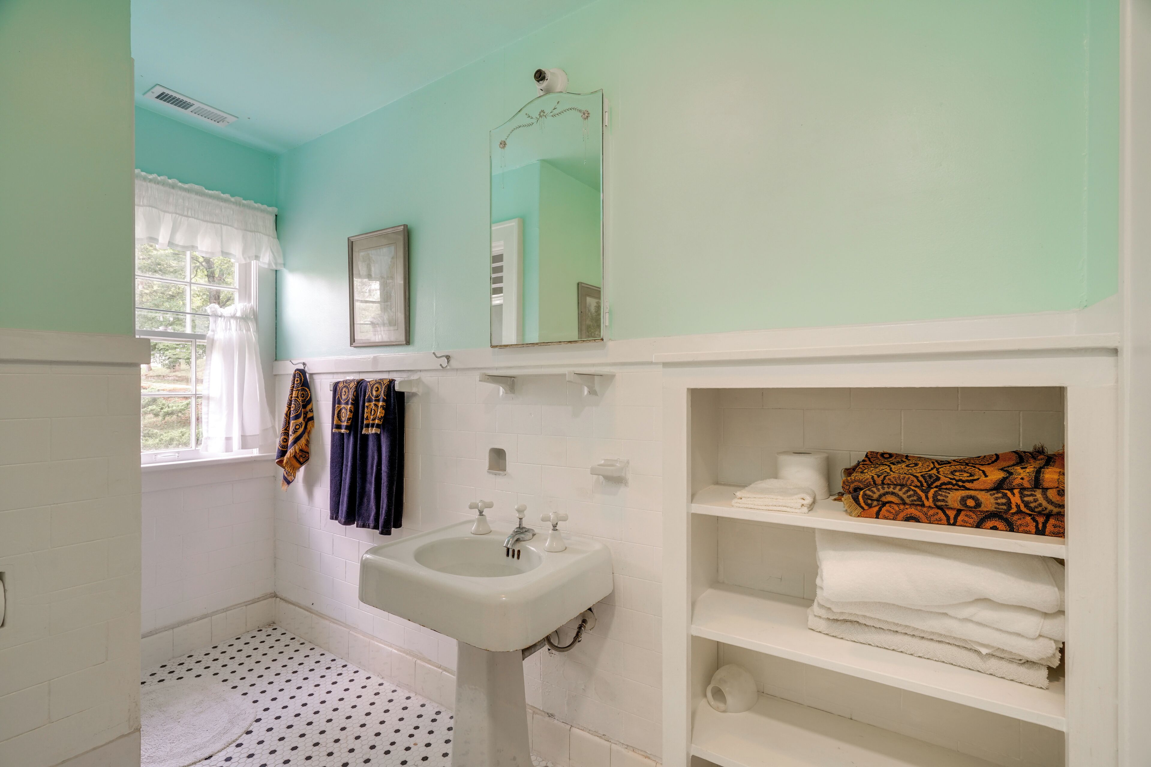 A bathroom with a white sink, a mirror, and a shelf with towels.