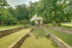 A small white building with a porch, surrounded by a stone wall and grassy area. - Ride, Swim & Hike! Kaolin Farms Cottage (Belleview)