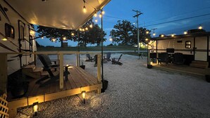 An RV with a covered deck area, outdoor seating, and string lights.