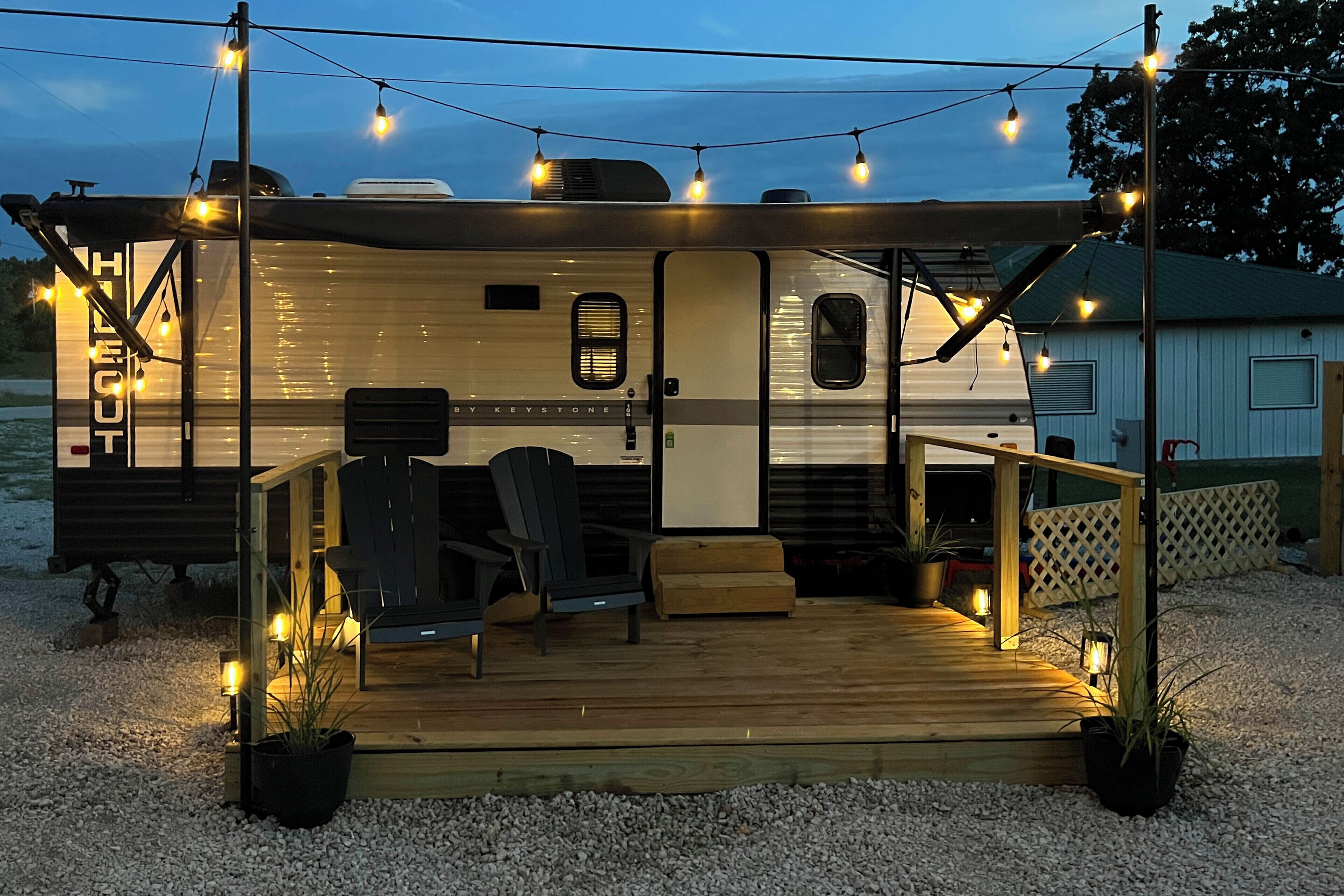 A recreational vehicle with a covered deck, seating area, and string lights.