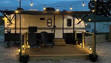 A recreational vehicle with a covered deck, seating area, and string lights.
