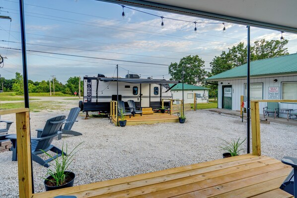 A recreational vehicle (RV) with a covered deck and outdoor seating area, a gravel parking lot, and a building with a green roof.