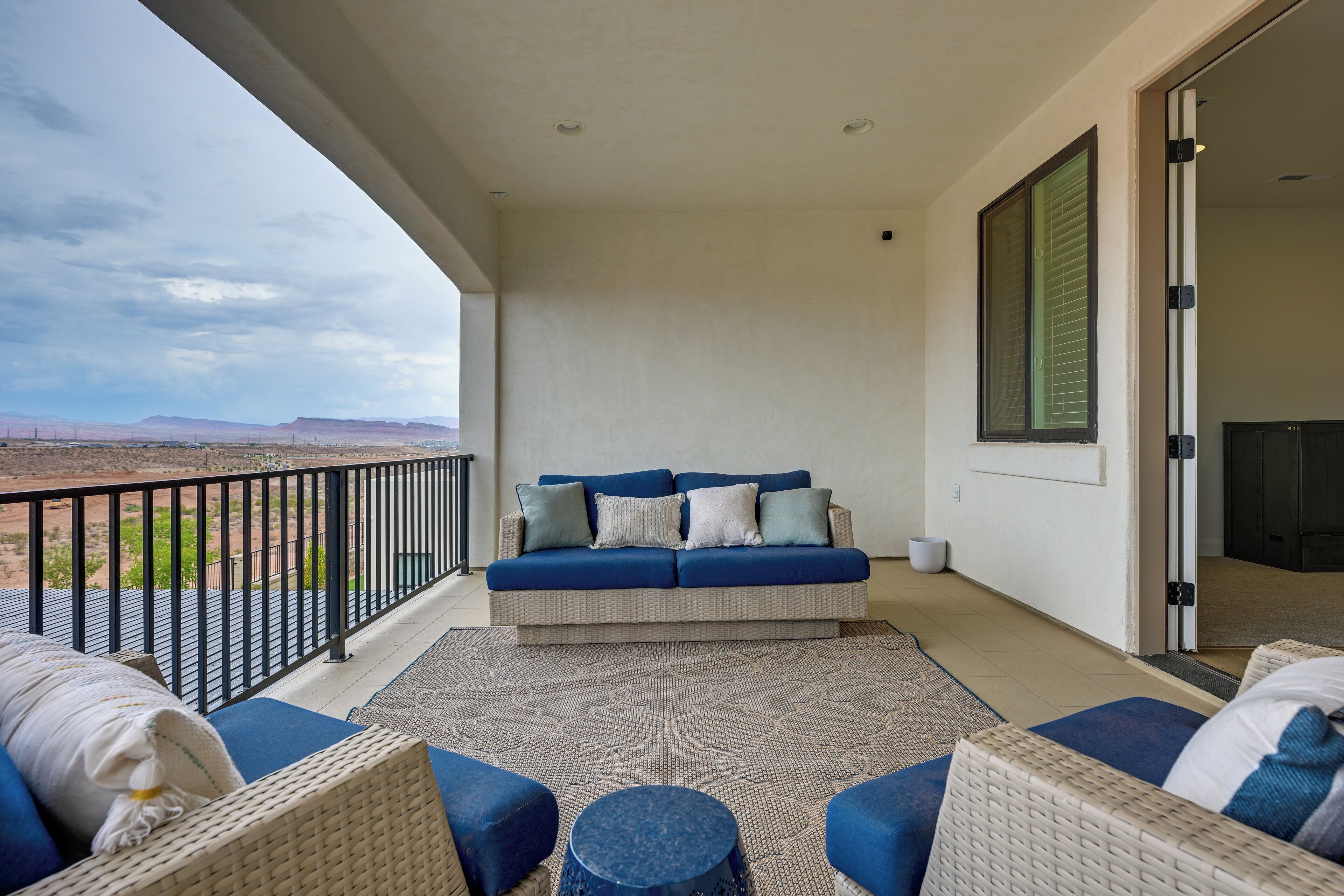 A balcony with a sofa and chairs, a view of the desert, and a door to the interior.