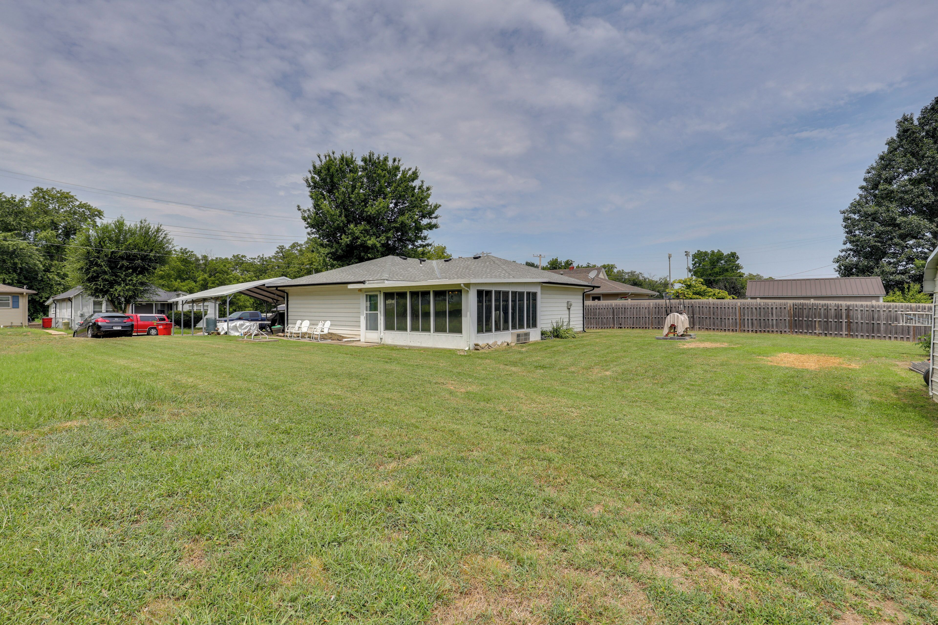 A residential backyard with a covered patio, a lawn, and a wooden fence.