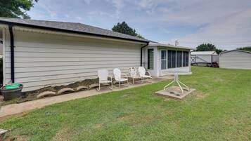 A single-story house with a covered patio area, a small table, and three white chairs.