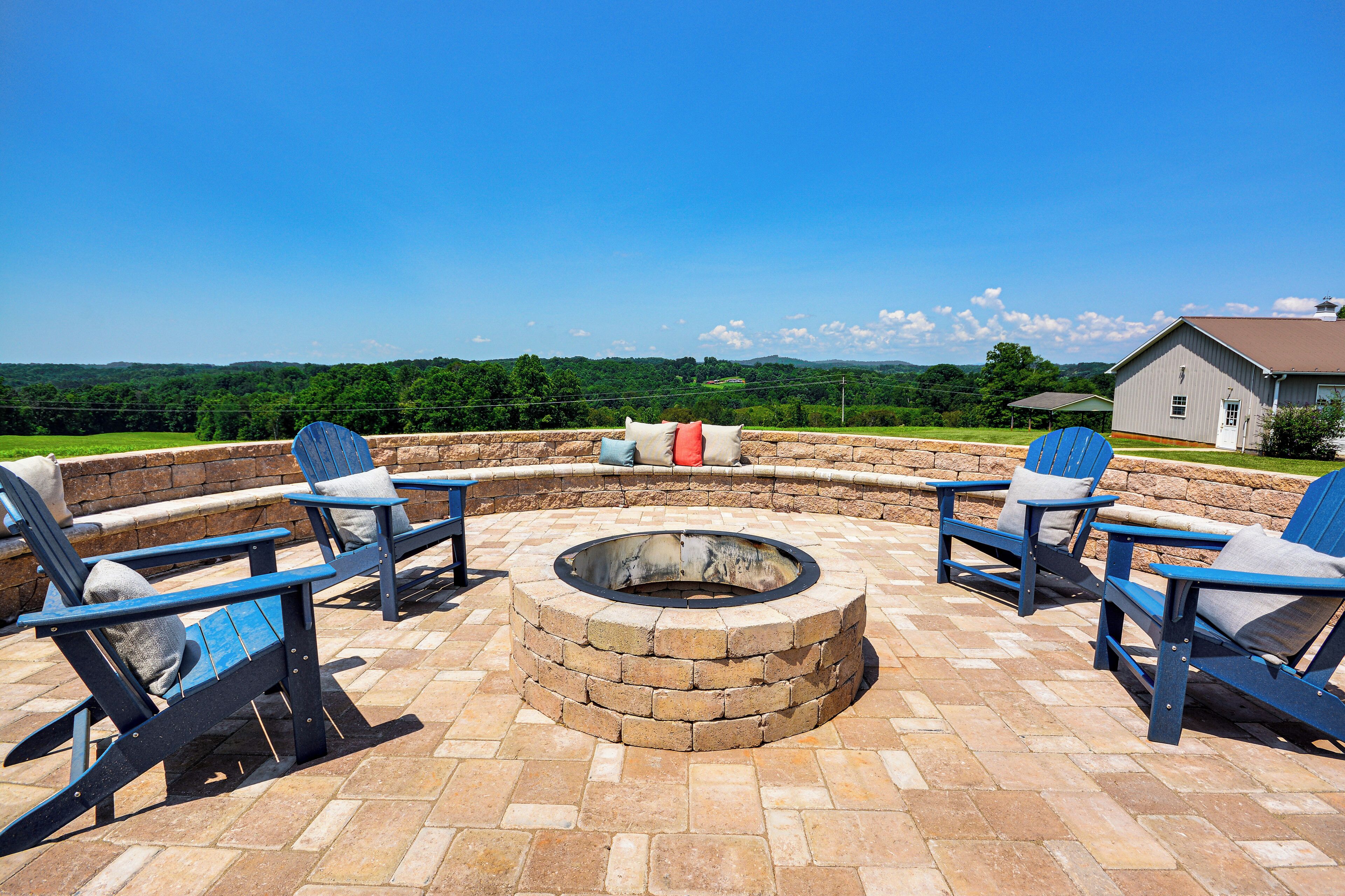 An outdoor seating area with a circular fire pit and blue Adirondack chairs.