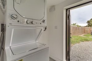 A front view of a white washing machine with control knobs and a door, positioned next to a door leading to an outdoor area with a wooden fence and gravel path. - FIU Basecamp: Miami Home w/ Fenced Yard! (Miami)