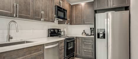 A modern kitchen with stainless steel appliances, wooden cabinets, and a white countertop.