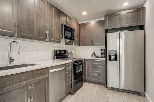 A modern kitchen with stainless steel appliances, wooden cabinets, and a white countertop. - FIU Basecamp: Miami Home w/ Fenced Yard! (Miami)