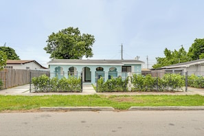 A single-story house with a light blue exterior, a front yard with a small fence, and a large tree. - FIU Basecamp: Miami Home w/ Fenced Yard! (Miami)
