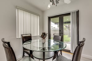 A dining area with a glass table surrounded by chairs, a potted plant, and a view through a sliding glass door. - FIU Basecamp: Miami Home w/ Fenced Yard! (Miami)