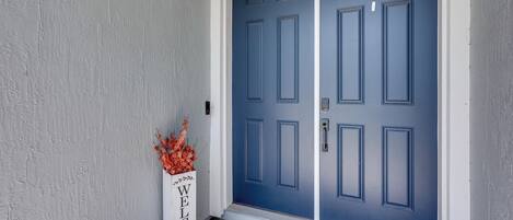 Una puerta azul con un cartel de bienvenida y un arreglo floral.