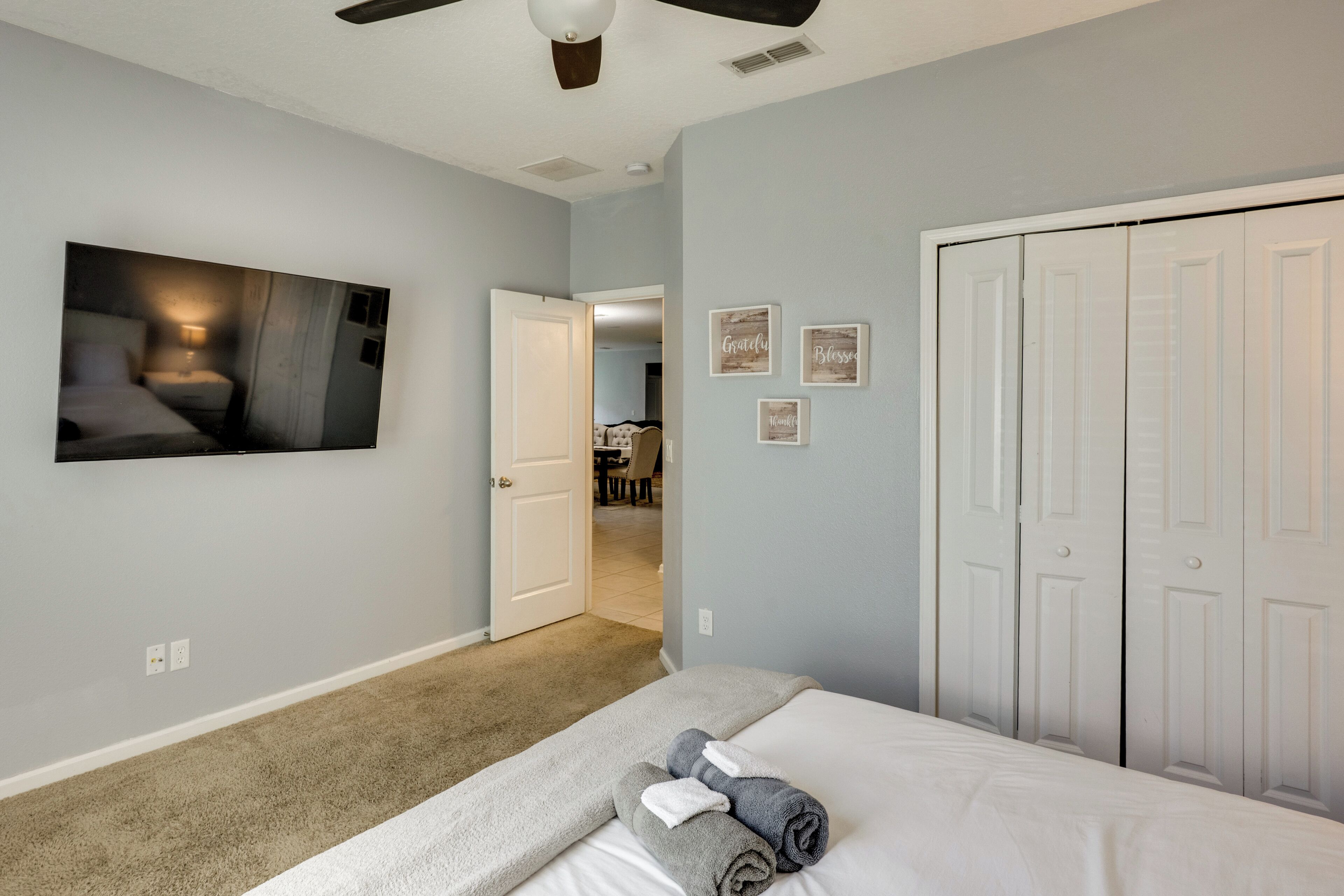 Un dormitorio con cama, ventilador de techo, un cuadro y un pasillo que lleva a un baño.