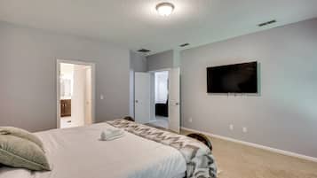 A bedroom with a bed, a television mounted on the wall, and a door leading to another room.