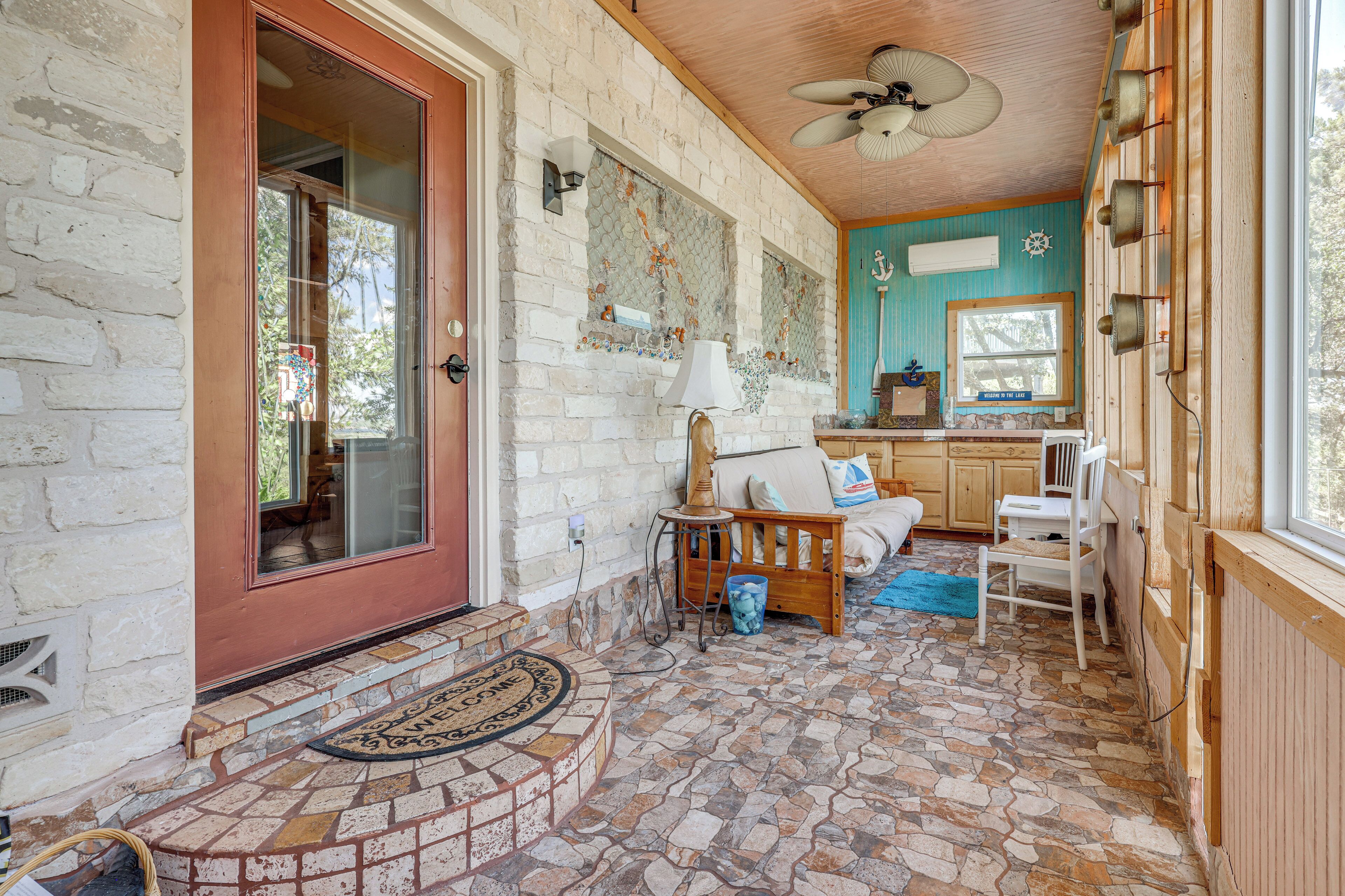 A cozy interior with a stone-tiled floor, a wooden bench, a white sofa, and a kitchen area with wooden cabinets.