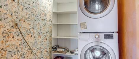 Een wasserette met een gestapelde wasmachine en droger, een plank met spelletjes en bloemenbehang.