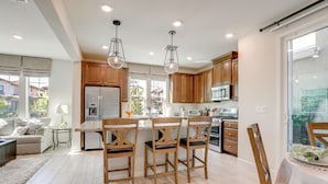 A modern kitchen with wooden cabinets, a stainless steel refrigerator, and a dining area with wooden chairs. - New Build w/ Patio! Roseville Extended Stay (Roseville)