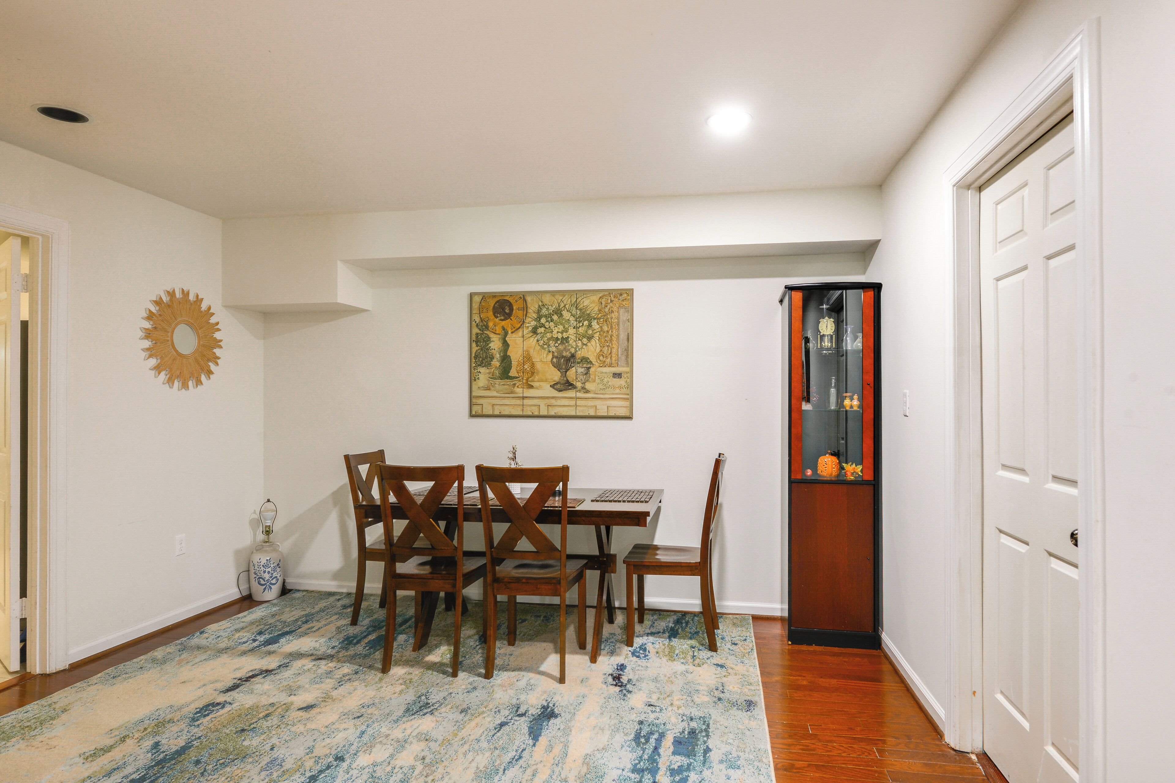 A dining area with a table and chairs, a painting on the wall, and a door with a mirror and clock.