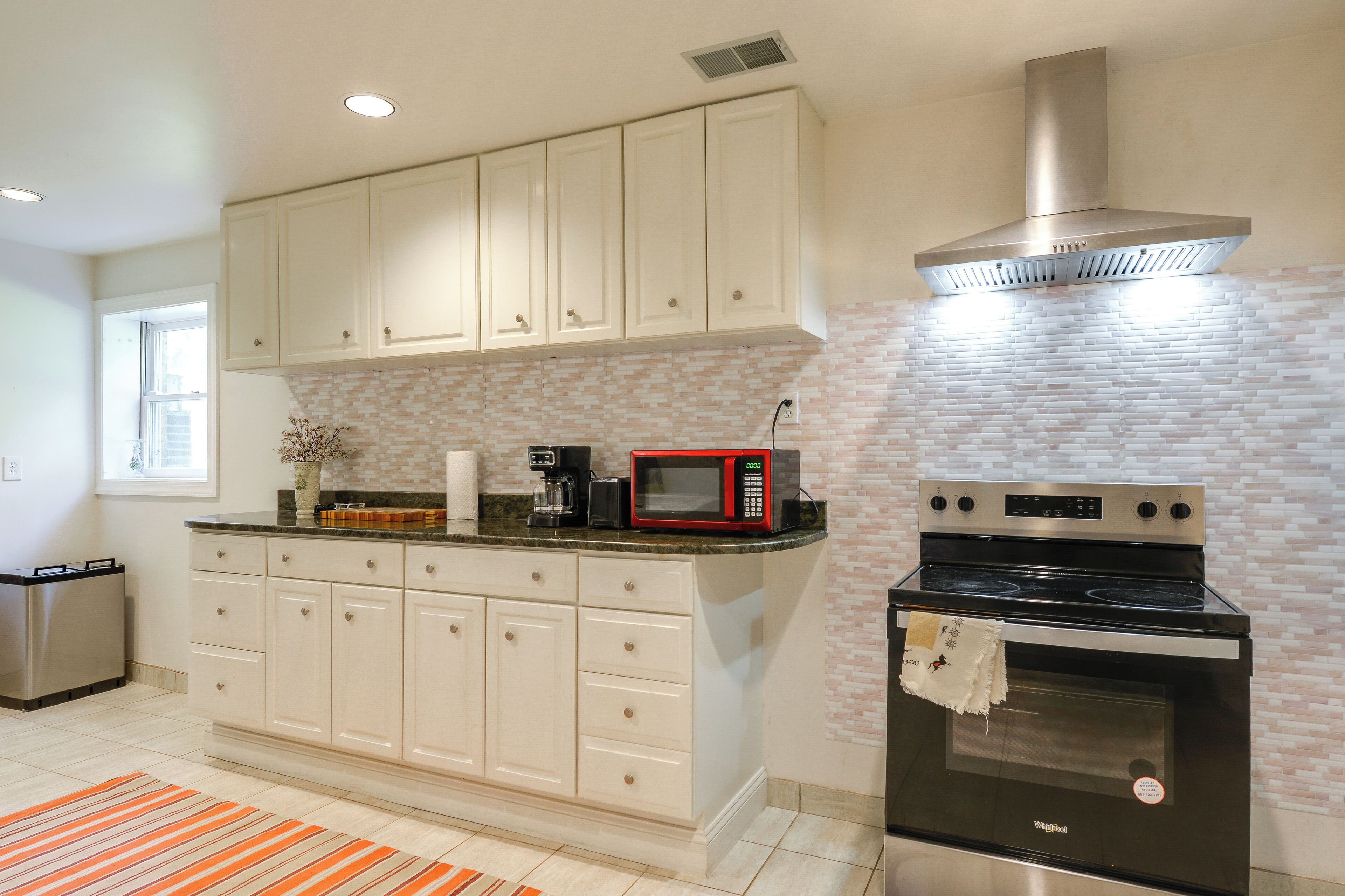 A modern kitchen with white cabinetry, a stainless steel range hood, a black stove, and a red microwave.