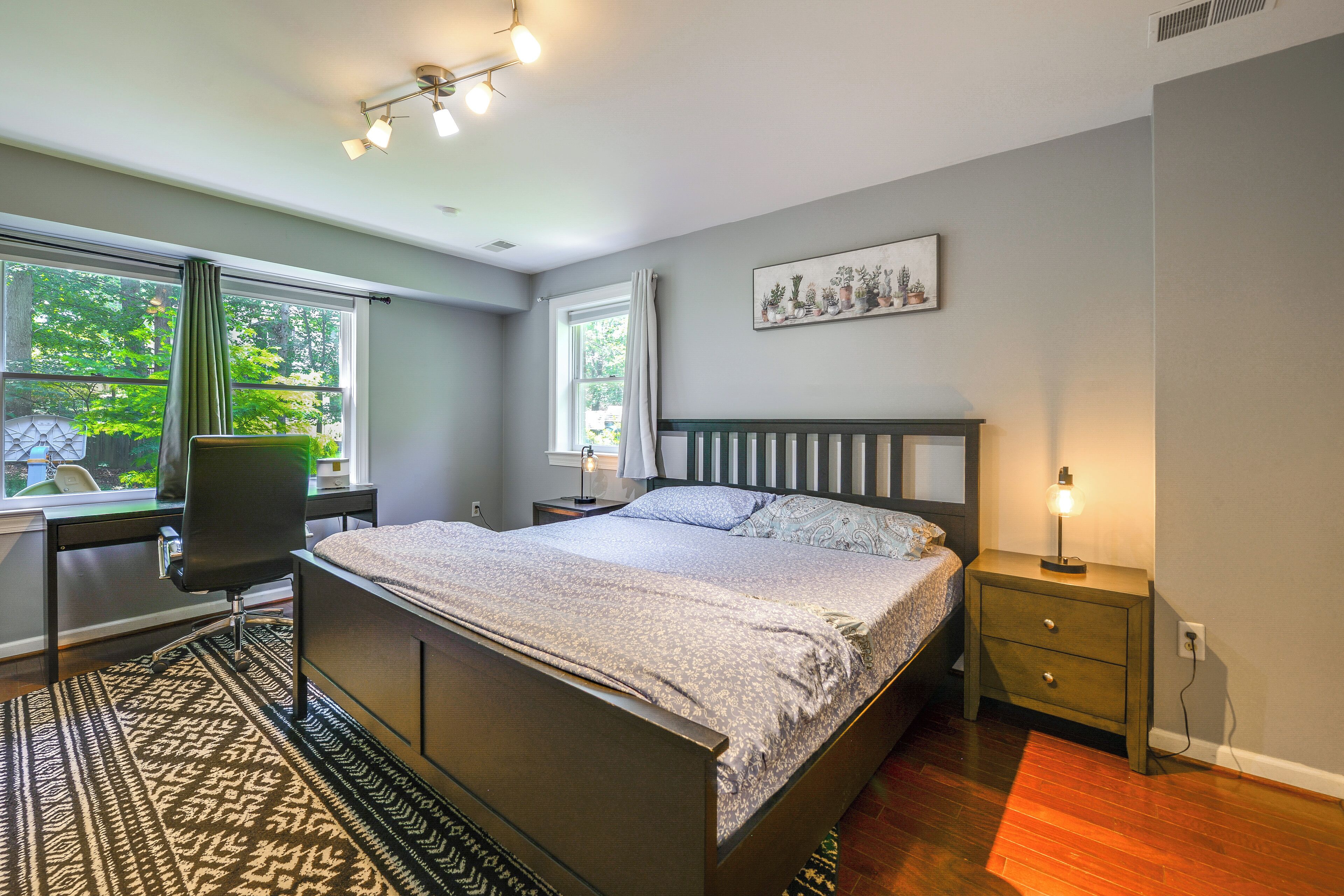 Quarto com cama, escrivaninha, cadeira, mesa de cabeceira e janela com cortinas.