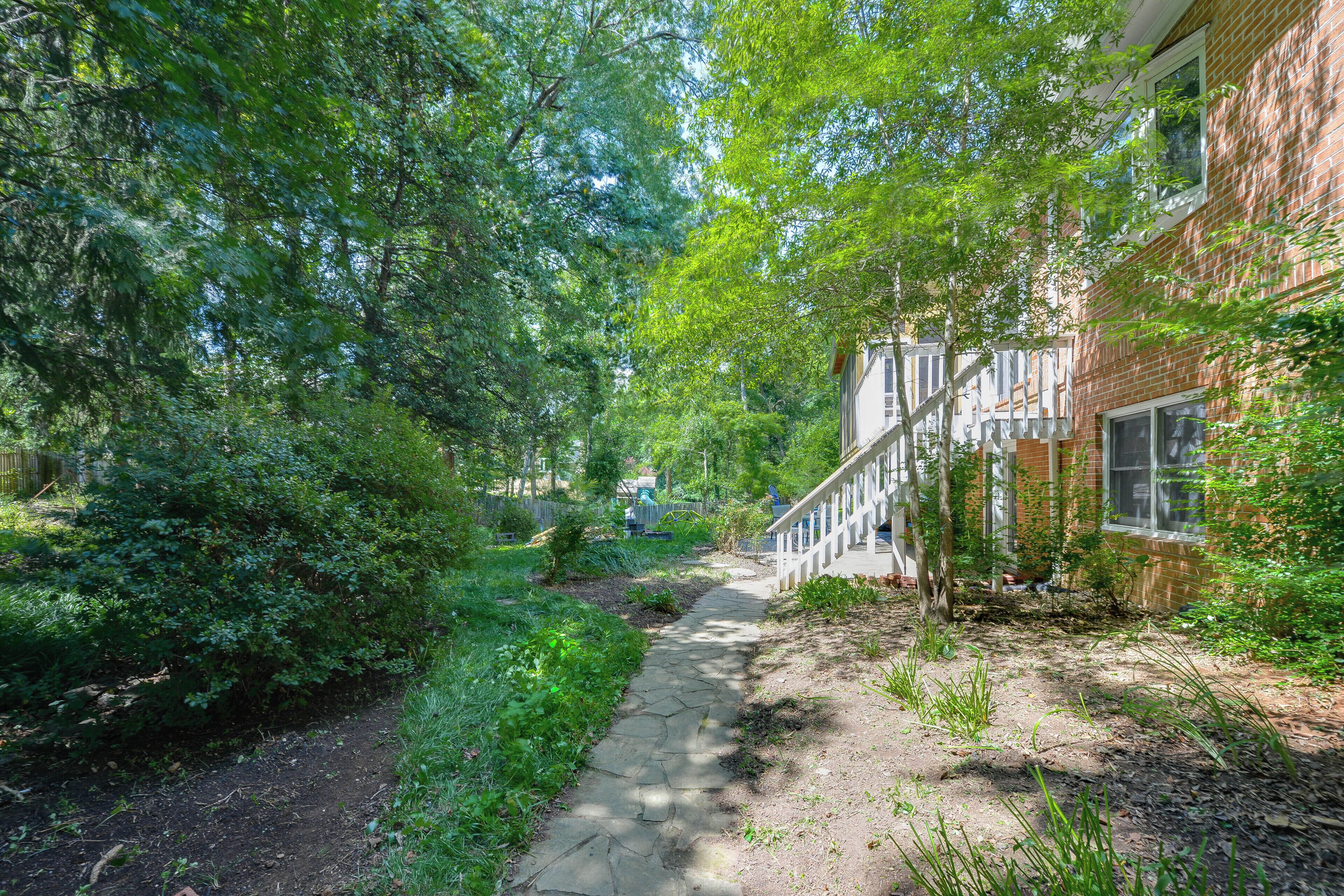A pathway leading through a garden area with dense foliage and a brick building on one side.