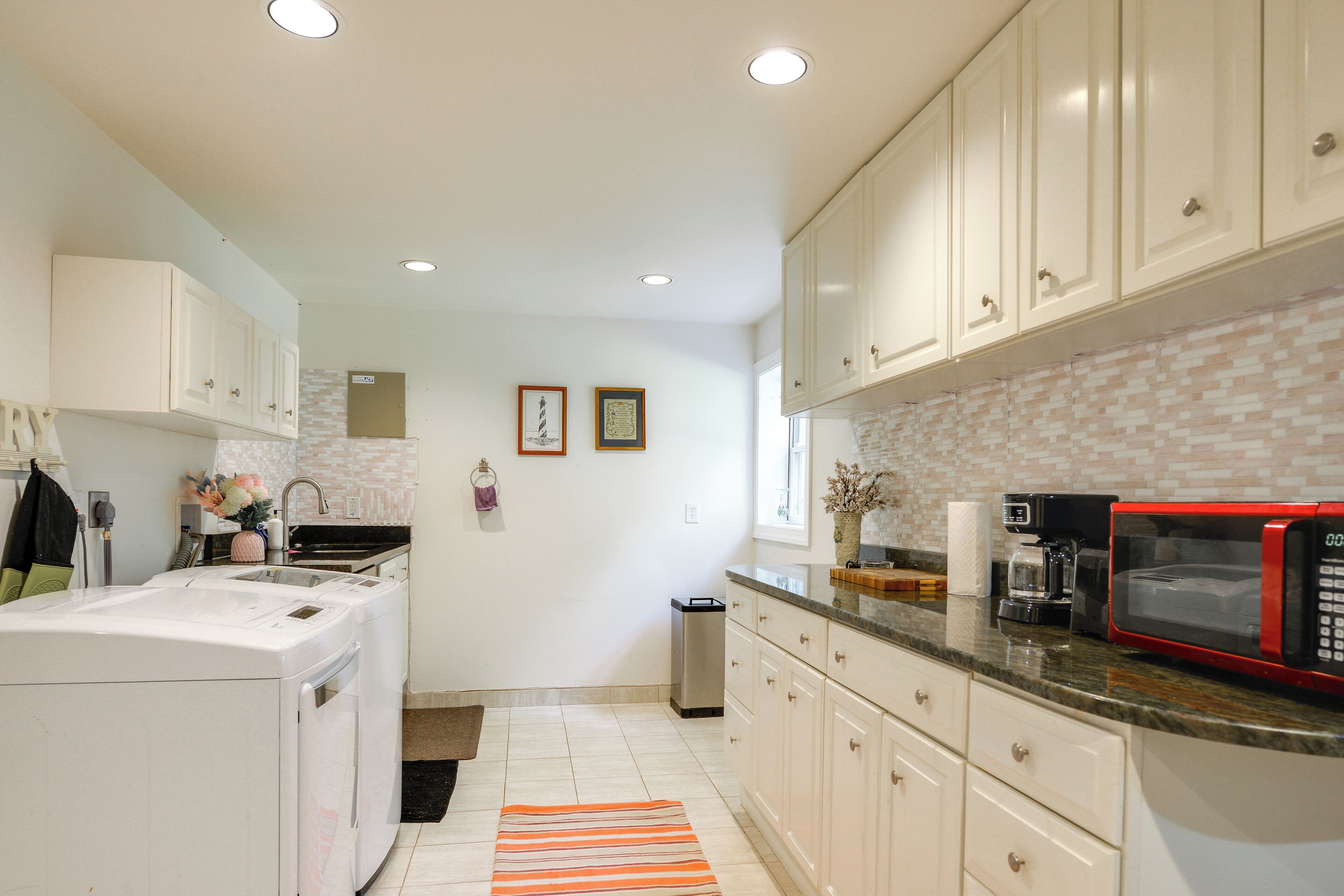 Una cocina con armarios blancos, un microondas rojo y salpicadero de azulejos.