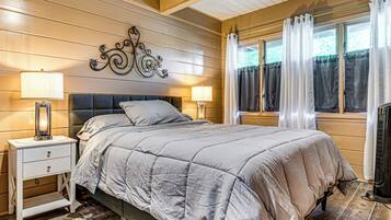 A bedroom with a bed, two bedside tables with lamps, a decorative wall piece, and a window with curtains.