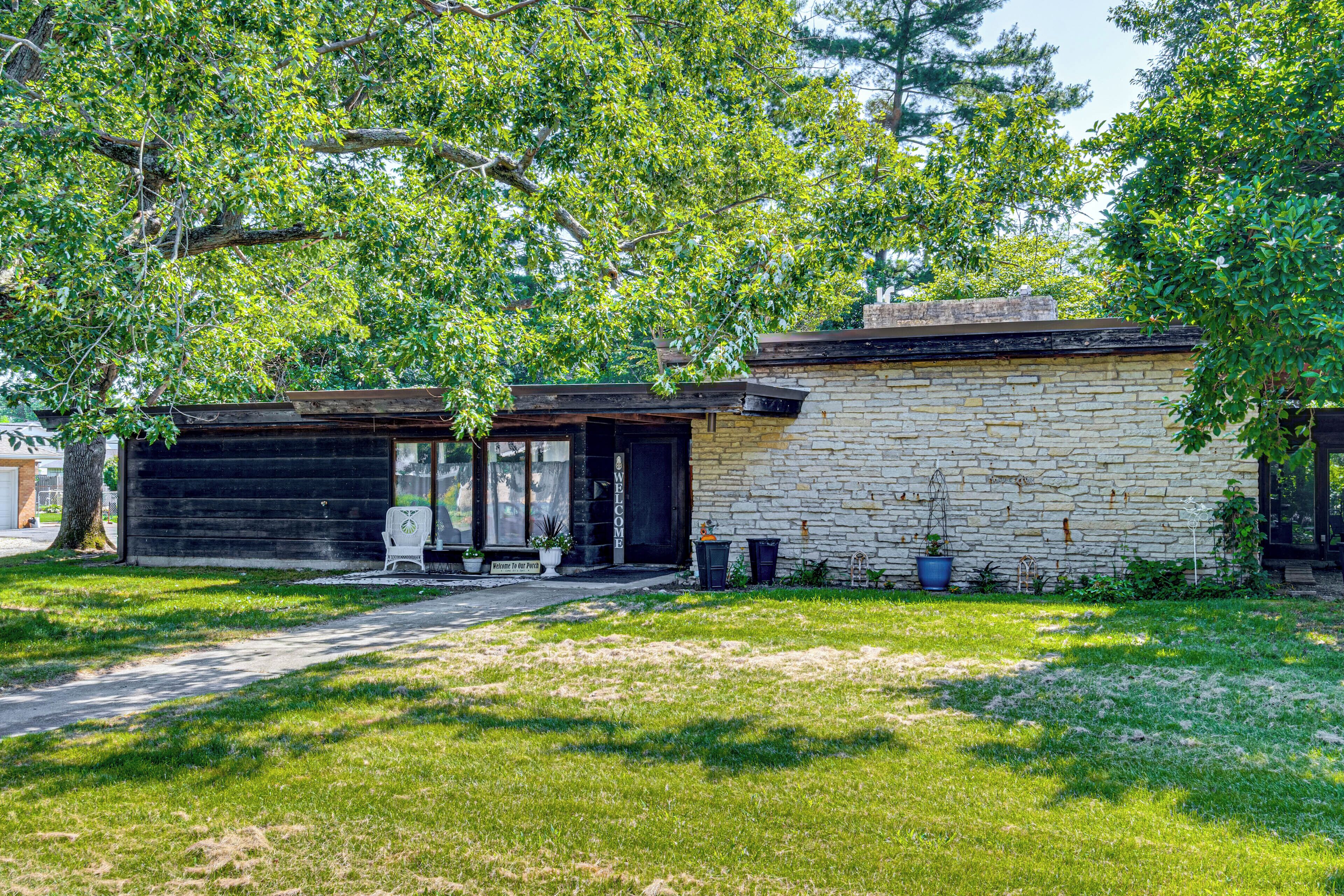 Un bâtiment en pierre de deux étages, doté d’un garage, entouré d’une pelouse bien entretenue et d’arbres.