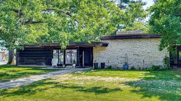 Un bâtiment en pierre de deux étages, doté d’un garage, entouré d’une pelouse bien entretenue et d’arbres.