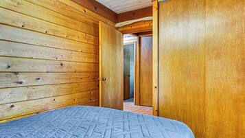 A wooden-paneled room with a bed, a door, and a visible hallway.