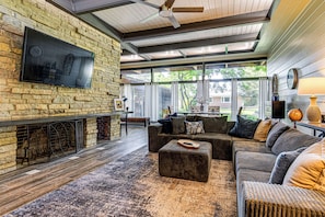 A living room with a stone fireplace, a flat-screen TV, and a large window. - Walk to Dtwn Rockville! Prairie-inspired Retreat (Rockville)