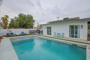 A swimming pool with lounge chairs, a small building with a glass door, and trees in the background.