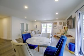 A modern living room with a round marble table, blue upholstered chairs, a beige sofa, and a large window with curtains. - Grill & Fire Pit! Palm Desert Extended Escape (Palm Desert)