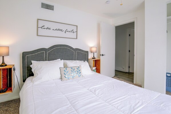 A neatly made bed with white linens, a decorative pillow, and a wall-mounted sign that reads 'love never fails'. - Grill & Fire Pit! Palm Desert Extended Escape (Palm Desert)