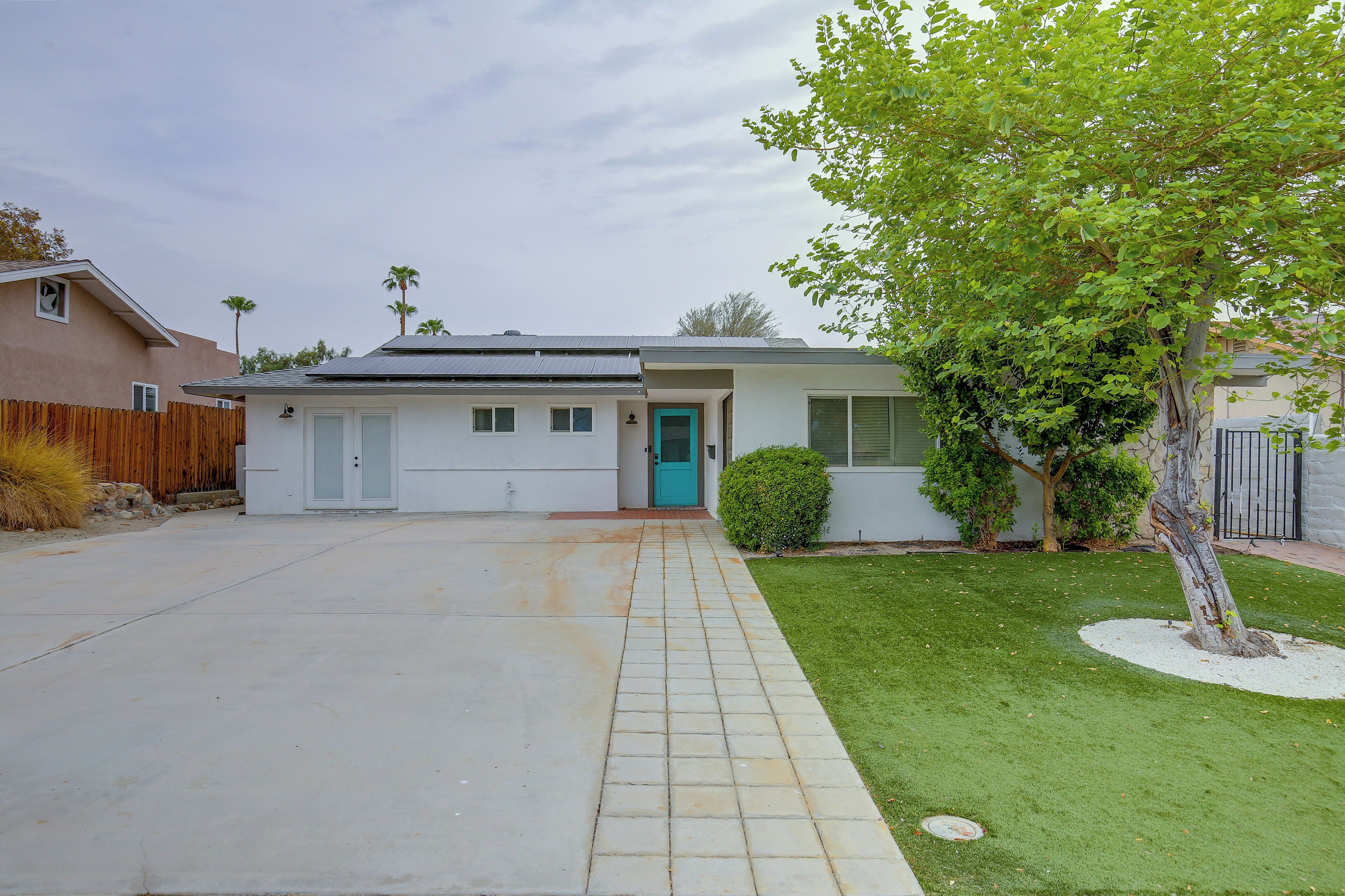 A single-story house with a garage, a front door, and a small front yard with a tree and a bush.