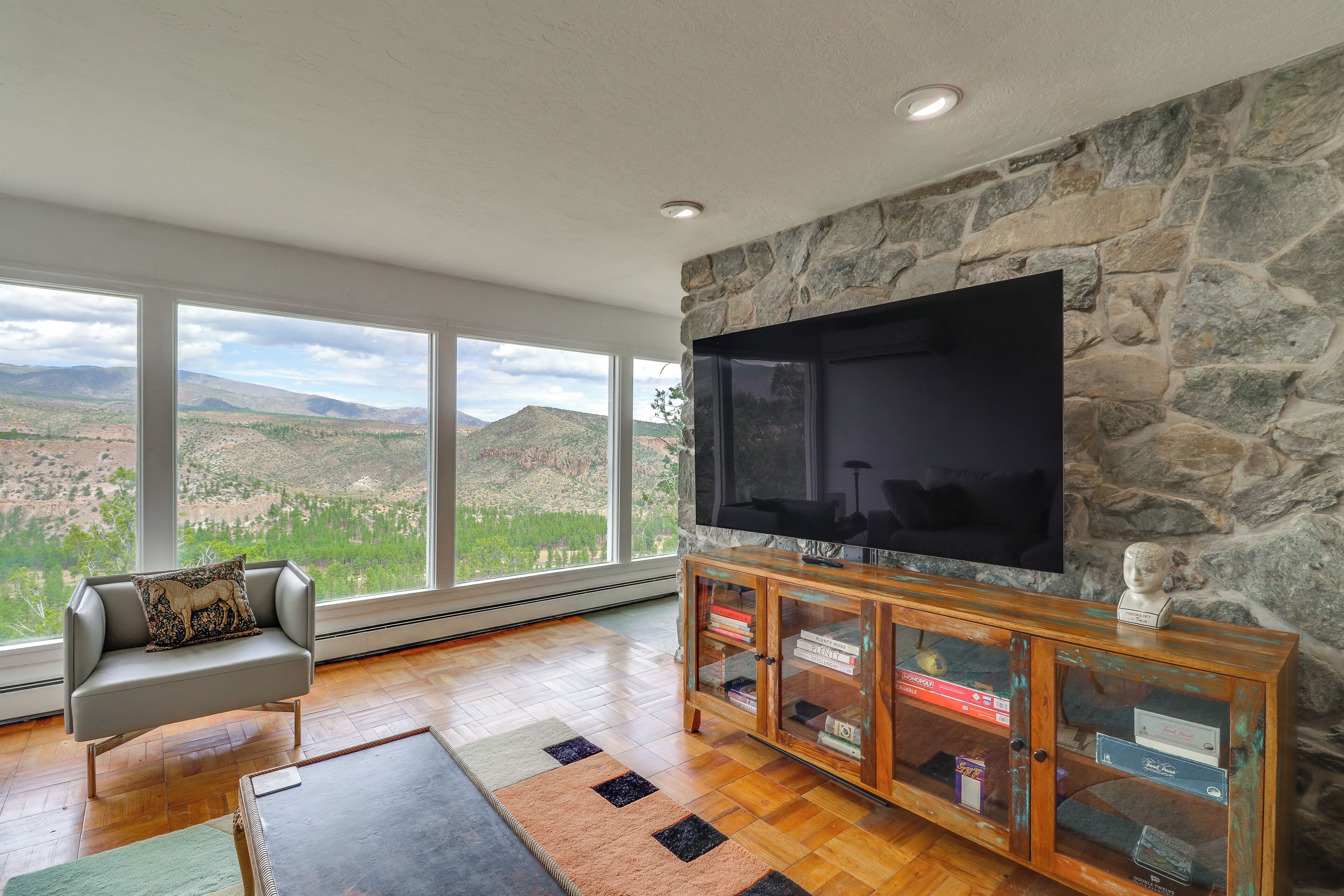 A living room with a stone wall, large windows, a flat-screen TV, a sofa, and a wooden entertainment unit.