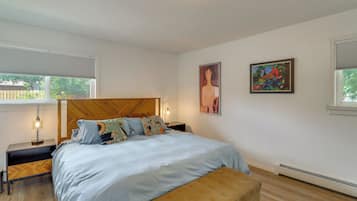 A bedroom with a bed, bedside tables, a bench, and two paintings.