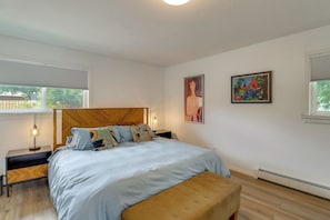 Quarto com uma cama, mesas de cabeceira, um banco e duas pinturas.