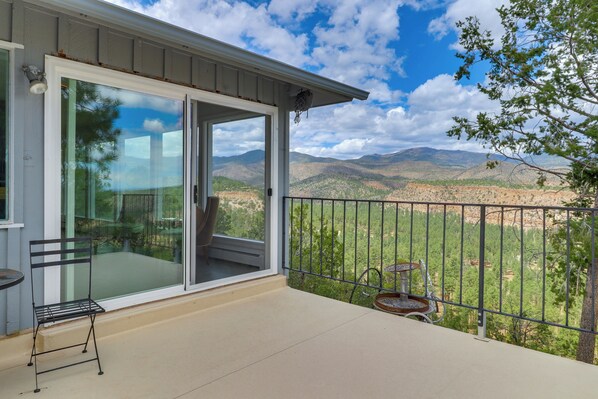 A balcony with a glass door leading to a patio area, a metal chair, and a small table. - Mid-century Home on Canyon-edge With Stellar Views (Los Alamos)