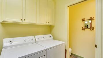 A laundry room with a front-loading washer and dryer, a mirror with a decorative frame, and a door leading to another room.