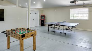 Une pièce avec une table de baby-foot, deux tables de ping-pong, une porte et une fenêtre.