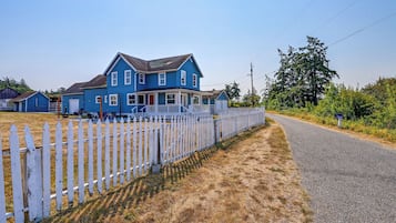 A two-story blue house with a white picket fence, a gravel driveway, and a clear sky.