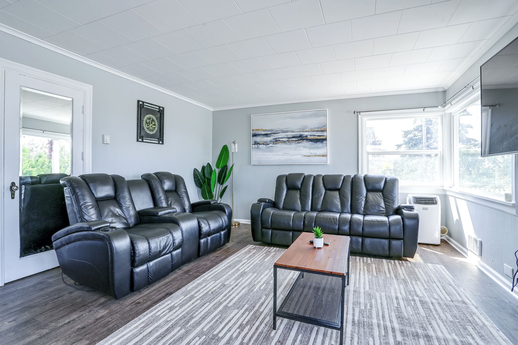 Ein modernes Wohnzimmer mit zwei schwarzen Ledersofas, einem Holztisch und einem großen, abstrakten Gemälde an der Wand.