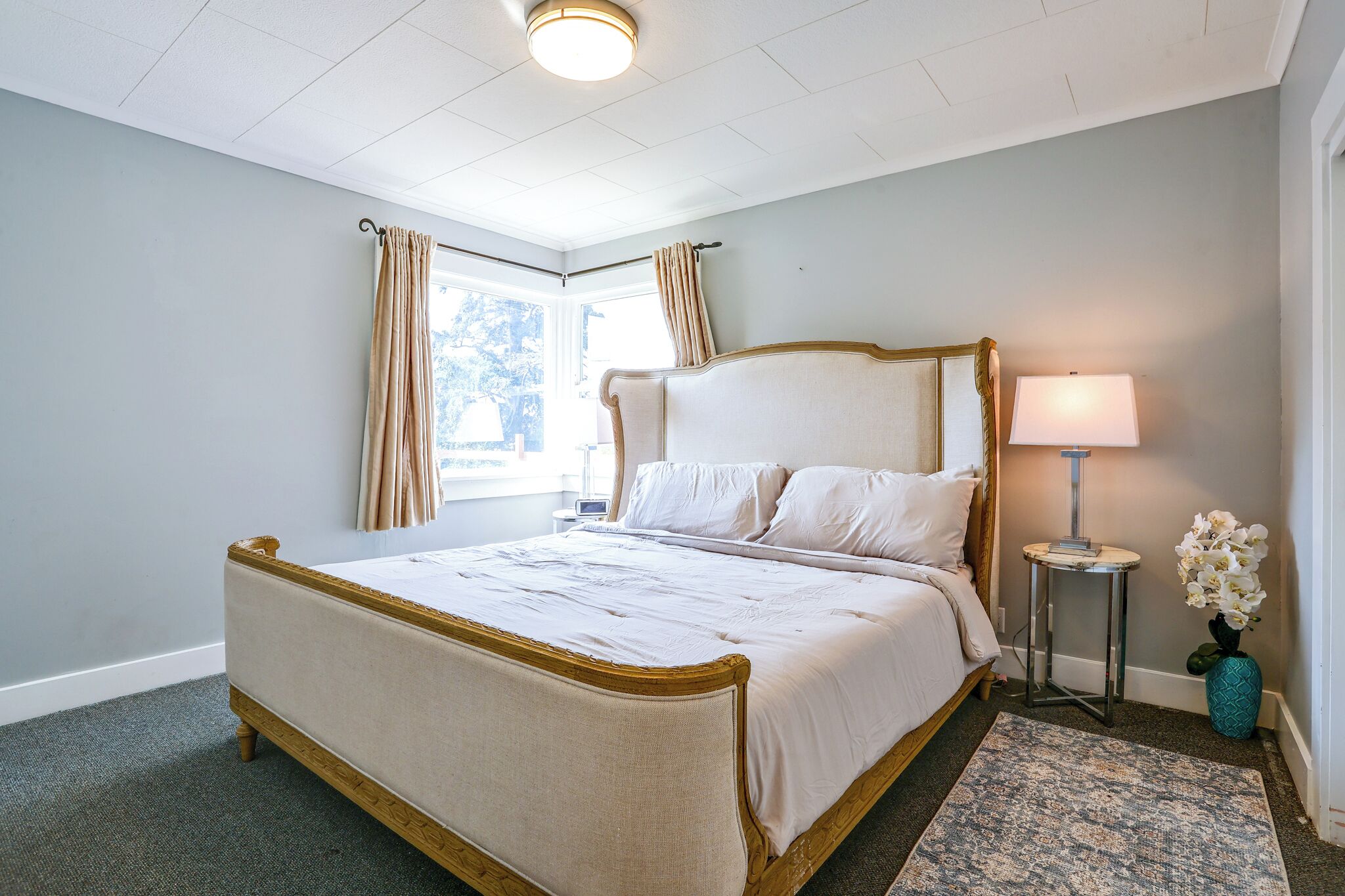 A hotel room with a large bed, a bedside table, a lamp, and a window with curtains.