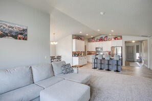 A modern living room with a grey sectional sofa, a kitchen with white cabinets, and a dining area with bar stools.
